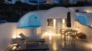 Un edificio moderno de forma abovedada, blanco, con piscina, sillones de descanso y zona de comedor.