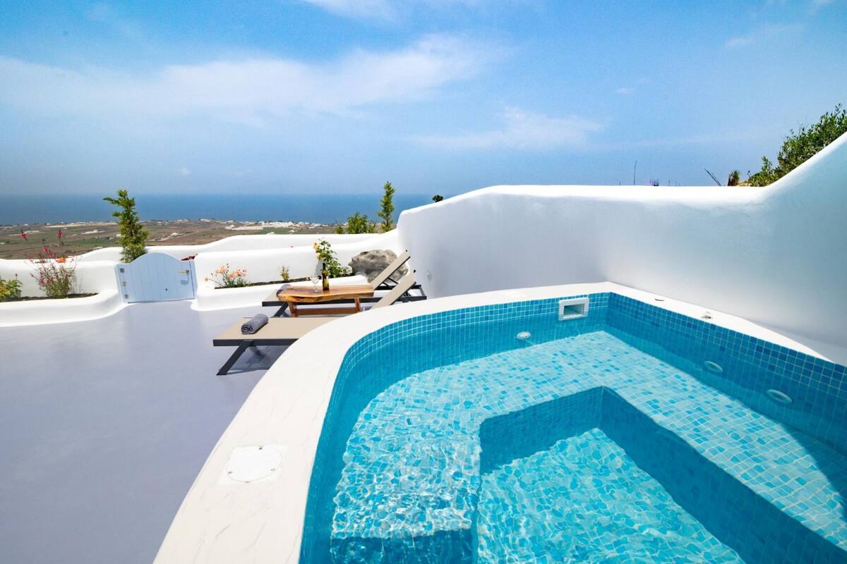 Zona de piscina con vista al mar, sillas de descanso y una estructura de paredes blancas.