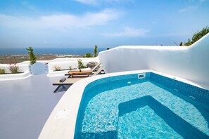 Zona de piscina con vista al mar, sillas de descanso y una estructura de paredes blancas.