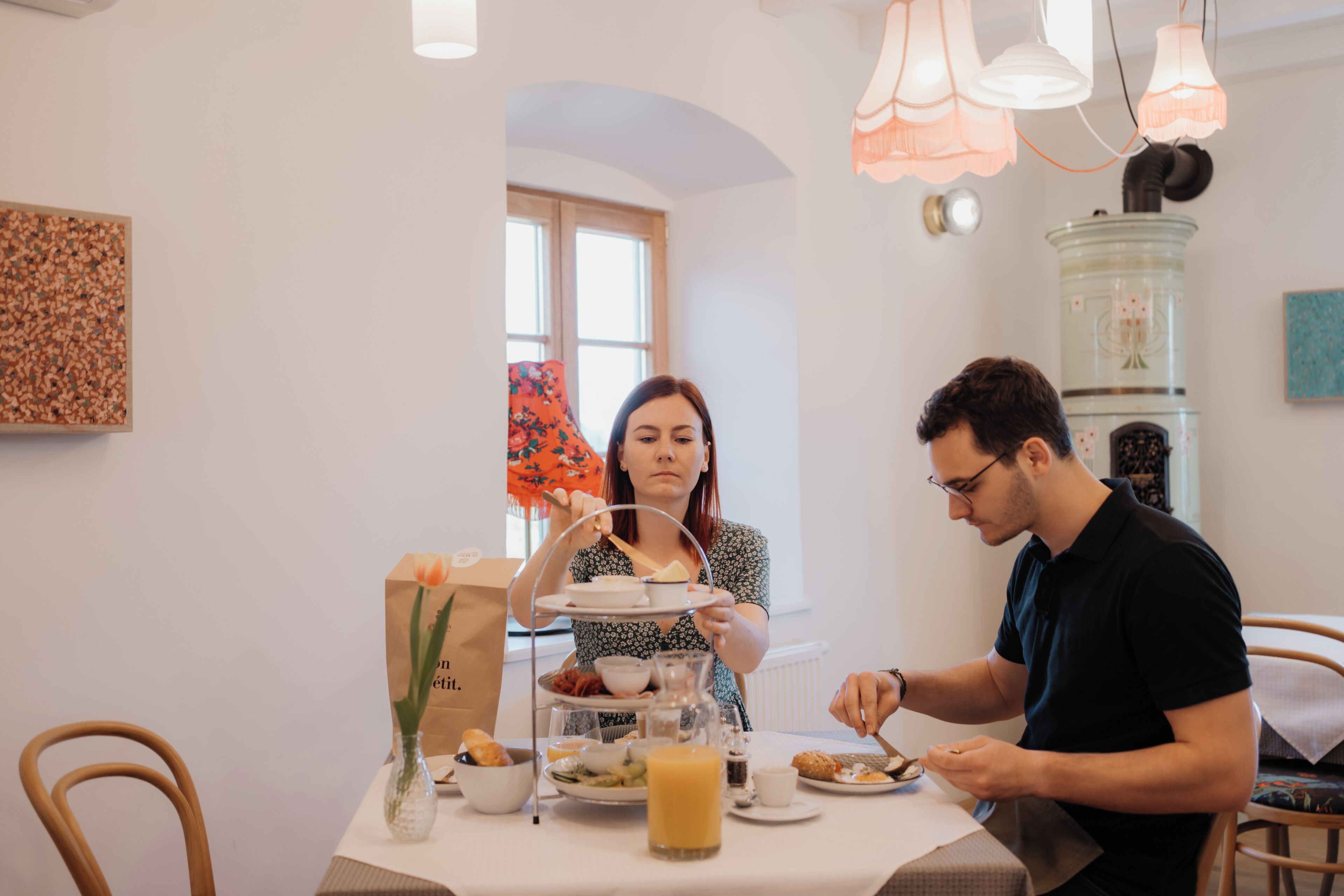 A dining table with a three-tiered tea service, a vase with a single flower, and a glass of orange juice.