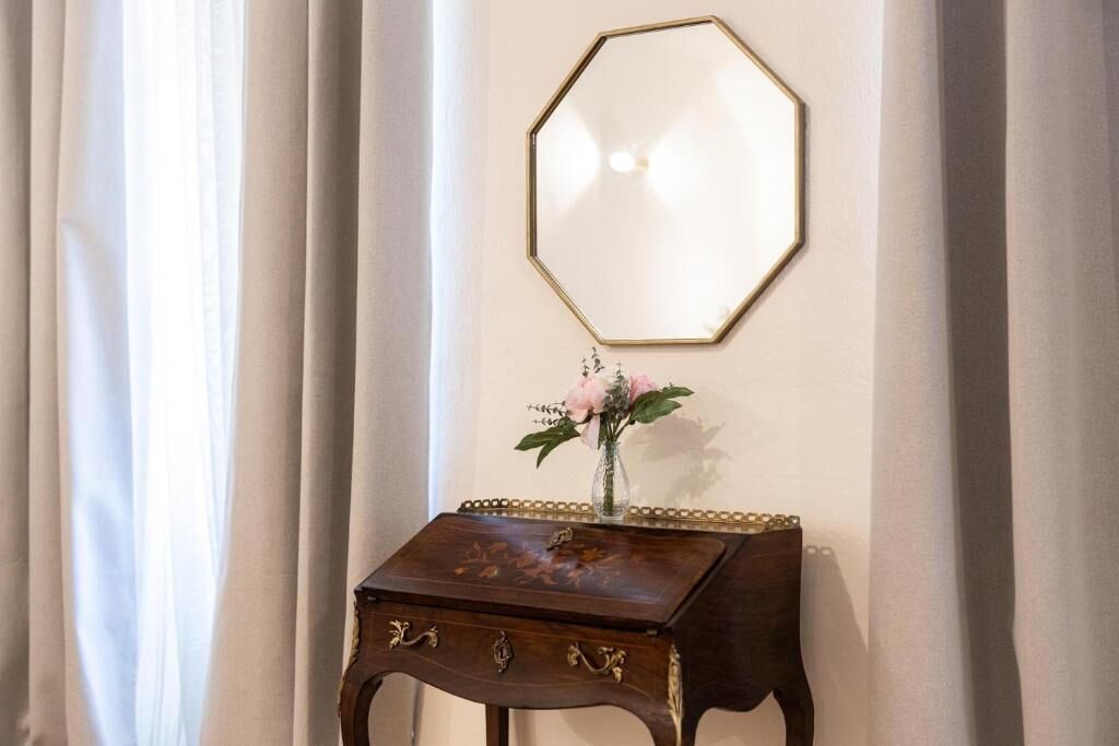 Una habitación con una mesita de madera, un florero con flores y un espejo octogonal fijado a la pared.
