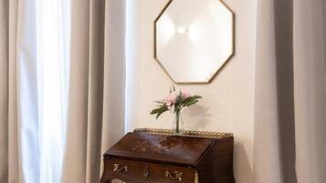 Una habitación con una mesita de madera, un florero con flores y un espejo octogonal fijado a la pared.