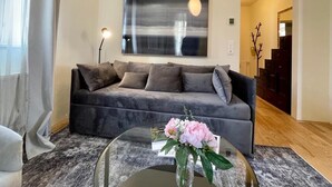 Ein modernes Wohnzimmer mit einem grauen Sofa, einem Glastisch mit Blumen und einem großen abstrakten Gemälde an der Wand.