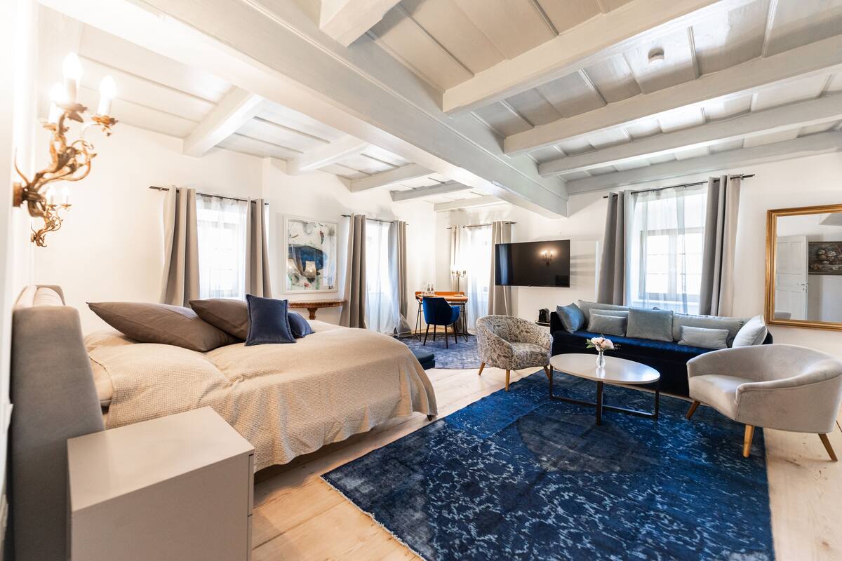 A modern hotel room with a bed, a sofa, a coffee table, and a TV.