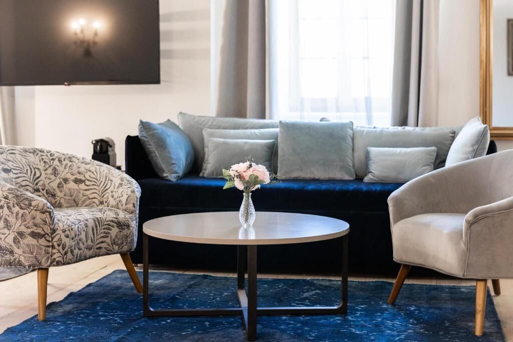 A living room with a dark blue sofa, patterned armchair, and a round coffee table with a vase of flowers.