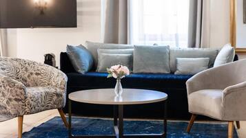 A living room with a dark blue sofa, patterned armchair, and a round coffee table with a vase of flowers.