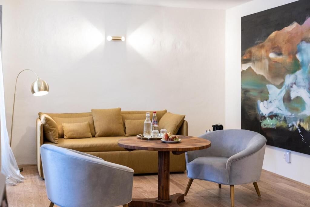 A modern living room with a sofa, two armchairs, a round wooden table, and a large abstract painting on the wall.