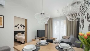 A modern hotel room with a dining area, a bed with a world map, a TV, and a sofa.