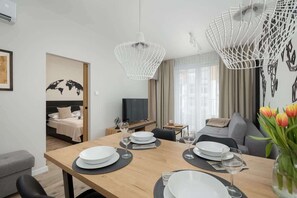 A modern hotel room with a dining area, a bed with a world map, a TV, and a sofa. - Tasteful Apartment | Balcony, Parking and Sauna (Kołobrzeg)