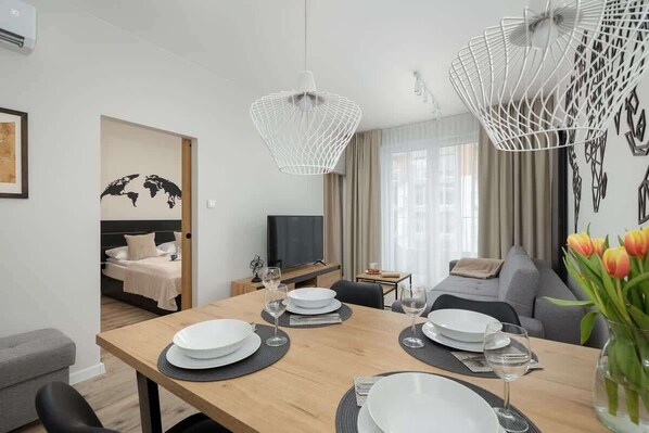 A modern hotel room with a dining area, a bed with a world map, a TV, and a sofa.