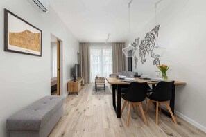 A modern living room with a dining area, a grey bench, a map artwork, and a hanging light fixture. - Tasteful Apartment | Balcony, Parking and Sauna (Kołobrzeg)