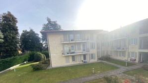 Un edifici residencial de diverses plantes amb balcons, un pati empedrat i vegetació als voltants.