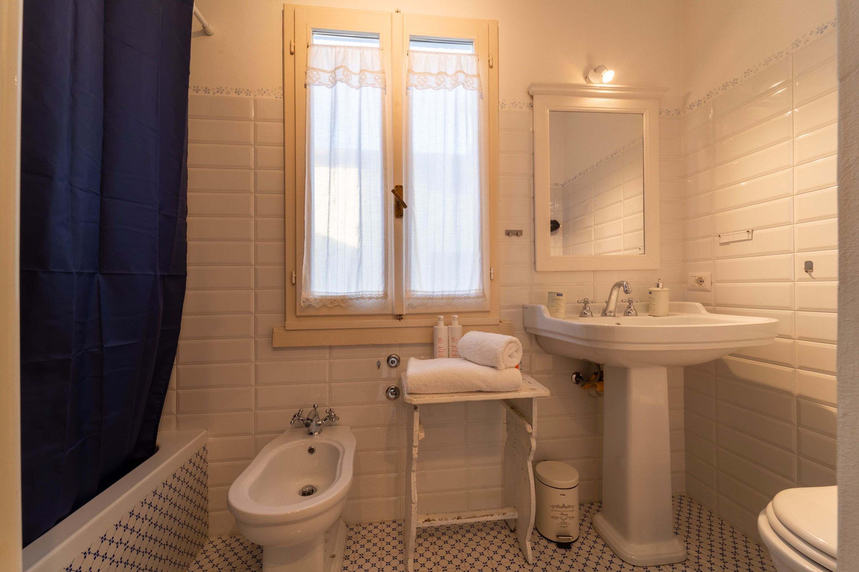 A bathroom with a bidet, toilet, sink, and a window with curtains.