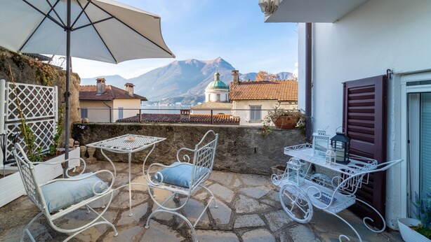 Un patio con una mesa y sillas, una sombrilla blanca, y vistas a edificios y montañas al fondo.