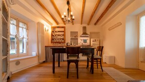 Un comedor con una mesa de madera, sillas y una araña. Se observa una cocina al fondo con estufa, fregadero y armarios.