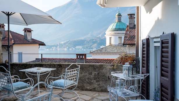 Une terrasse avec des sièges extérieurs, une vue sur une montagne et un bâtiment surmonté d’un dôme.