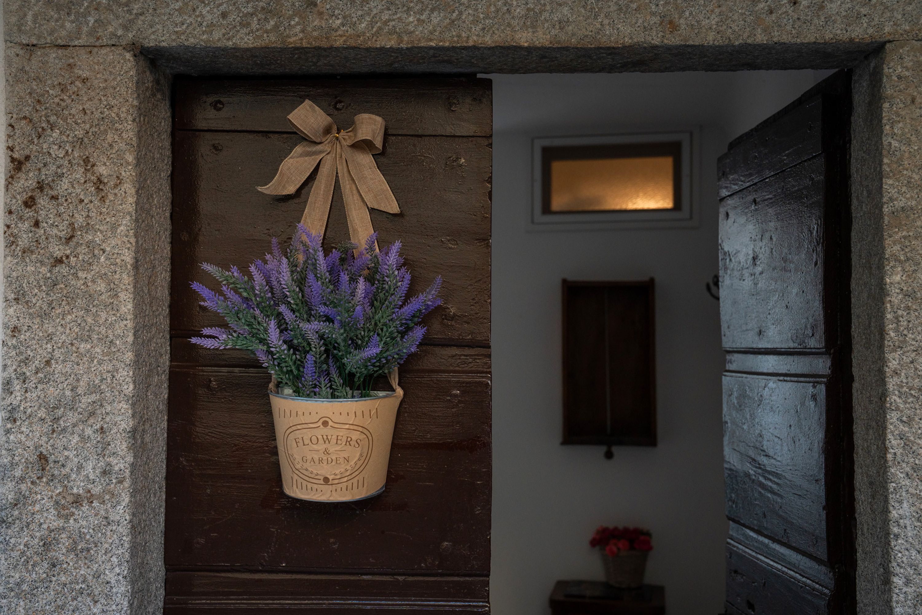 A wooden door with a hanging planter of lavender, a bow, and a sign reading "Flowers & Garden".