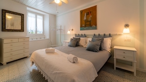 Une chambre à coucher comprenant un lit, des tables de chevet, une commode, un ventilateur de plafond et un tableau accroché au mur.