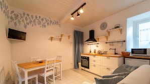 Une cuisine compacte avec des meubles blancs, une table à manger en bois et un four encastré.