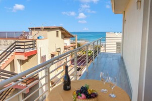 Un balcon avec une table, une bouteille et des verres, donnant sur une plage et des immeubles.
