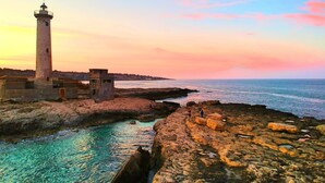 A coastal scene with a lighthouse, rocky shoreline, and calm sea. - Casa Golf a 200m From The Sea (Augusta)