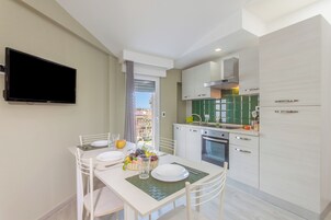 A modern kitchen with white cabinetry, a flat-screen TV mounted on the wall, and a dining area with a table set for two.