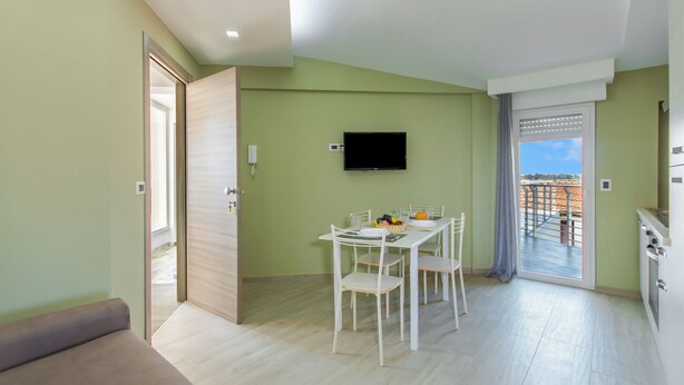 A modern apartment with a dining area, a TV mounted on the wall, and a balcony with a view. - Casa Golf a 200m From The Sea (Augusta)