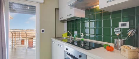A modern kitchen with a sliding glass door, a stainless steel range hood, and a green tiled backsplash.