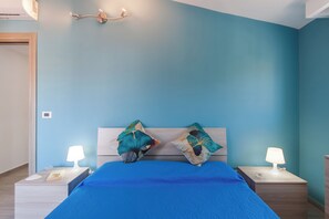 A bedroom with a bed, two bedside tables, a nightstand, a wall-mounted light fixture, and a door. - Casa Golf a 200m From The Sea (Augusta)
