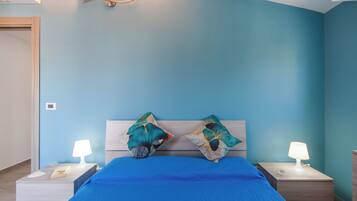 Un dormitorio con una cama, dos mesitas de noche, una lámpara de pared y una puerta.
