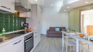 A modern kitchen with white cabinets, a green backsplash, and a dining area with a table set for four. - Casa Golf a 200m From The Sea (Augusta)