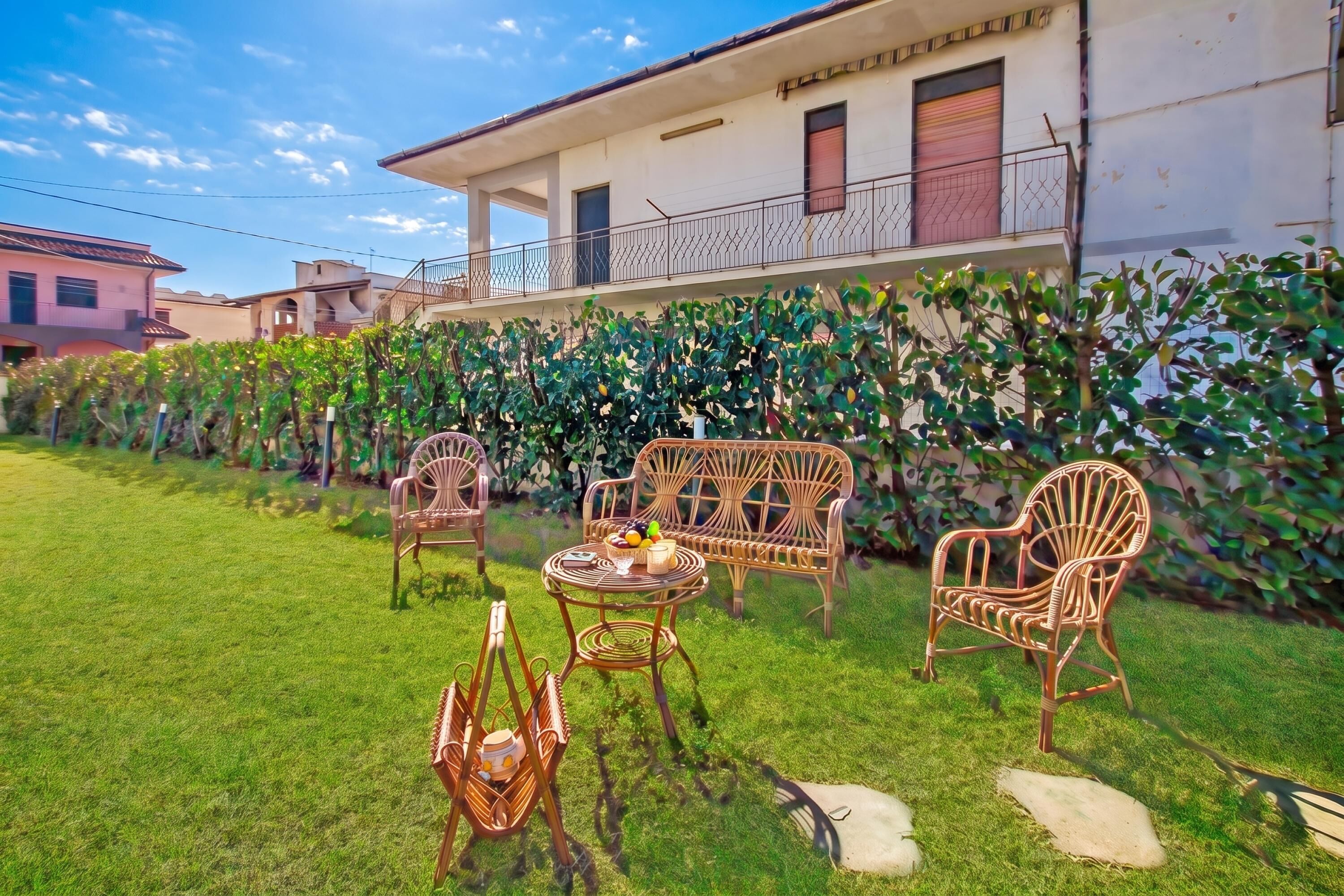 A grassy outdoor area with wicker furniture, a table with fruits, and a building with balconies in the background.