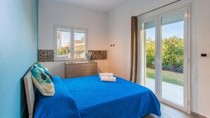 A bedroom with a bed, a window, a mirror, a nightstand, and a sliding glass door leading to an outdoor area.