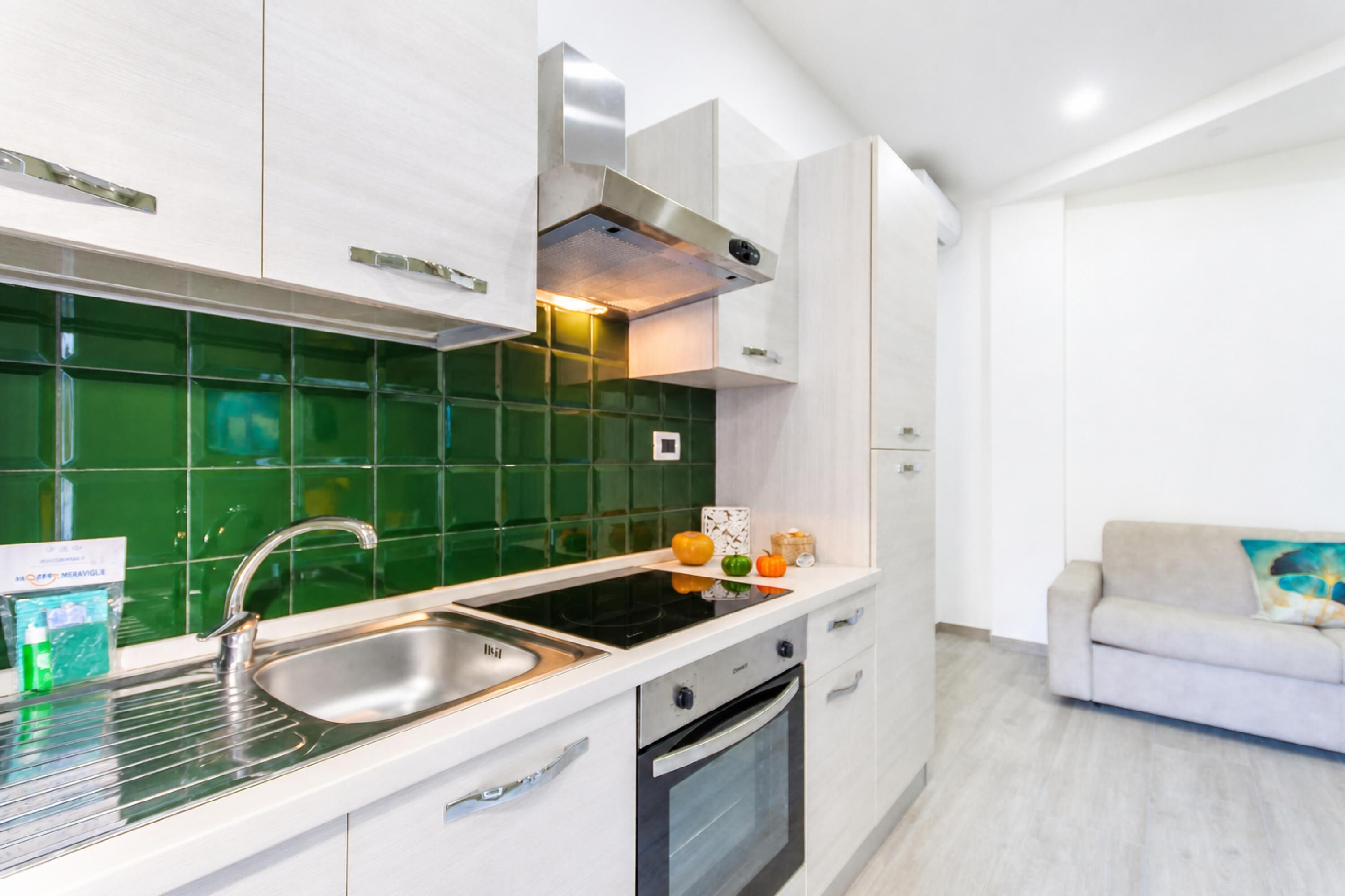 A modern kitchen with a stainless steel sink, a built-in oven, and a green backsplash.