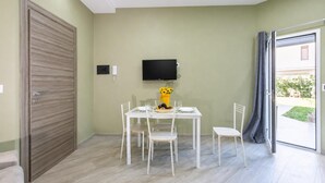 A room with a dining table, chairs, a TV mounted on the wall, and a sliding glass door leading to an outdoor area.
