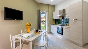A modern kitchen with white cabinets, a flat-screen TV mounted on the wall, and a dining area with a table set for two.