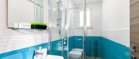 Un baño moderno con mampara de vidrio, lavamanos blanco y pared con azulejos azules.
