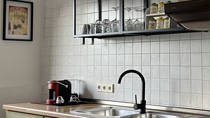 A kitchen with a black shelf holding glassware and jars, a coffee maker, and a sink with a black faucet. - "fewo Fuchs" im Ferienhaus am Tal Josaphat (Limburg an der Lahn)