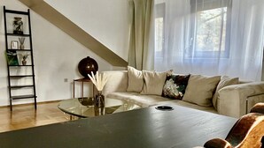 A modern living room with a large dark table, a beige sofa, and a glass coffee table. There is a ladder against the wall and a window with sheer curtains. - "fewo Fuchs" im Ferienhaus am Tal Josaphat (Limburg an der Lahn)