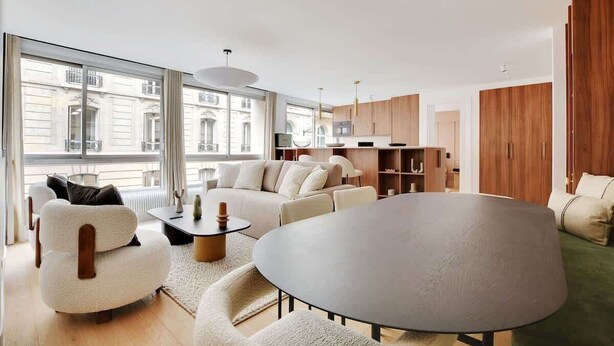 A modern living room with a round table, sofas, and a view of a cityscape through large windows. - A Breathtaking 3-BR/3BA in Trocadéro - Tour Eiffel (Paris)