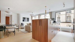 A modern kitchen with a central island, a dining area with a round table, and a living room with a sofa and a TV. - A Breathtaking 3-BR/3BA in Trocadéro - Tour Eiffel (Paris)
