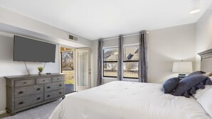 A bedroom with a large bed, a dresser, a TV mounted on the wall, and a window with curtains. - 2-bedroom, 2-bathroom in the heart of Branson, MO. Walk-in Unit.




 (Branson)