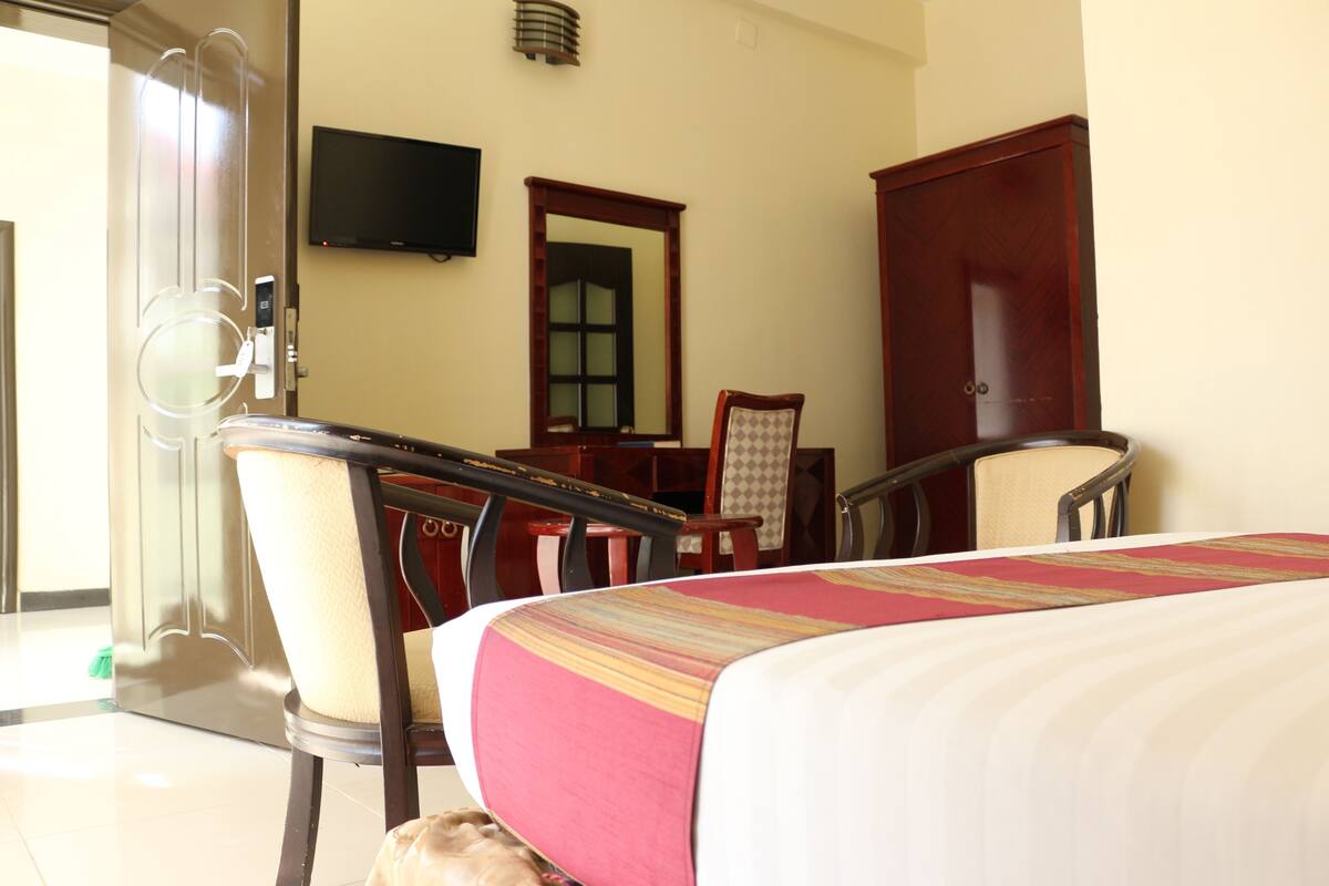 A hotel room with a bed, a desk, a chair, a television, and a wardrobe.