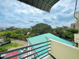 Vista desde un balcón con barandilla de metal, sobre un área verde con árboles y un edificio de techo azul.