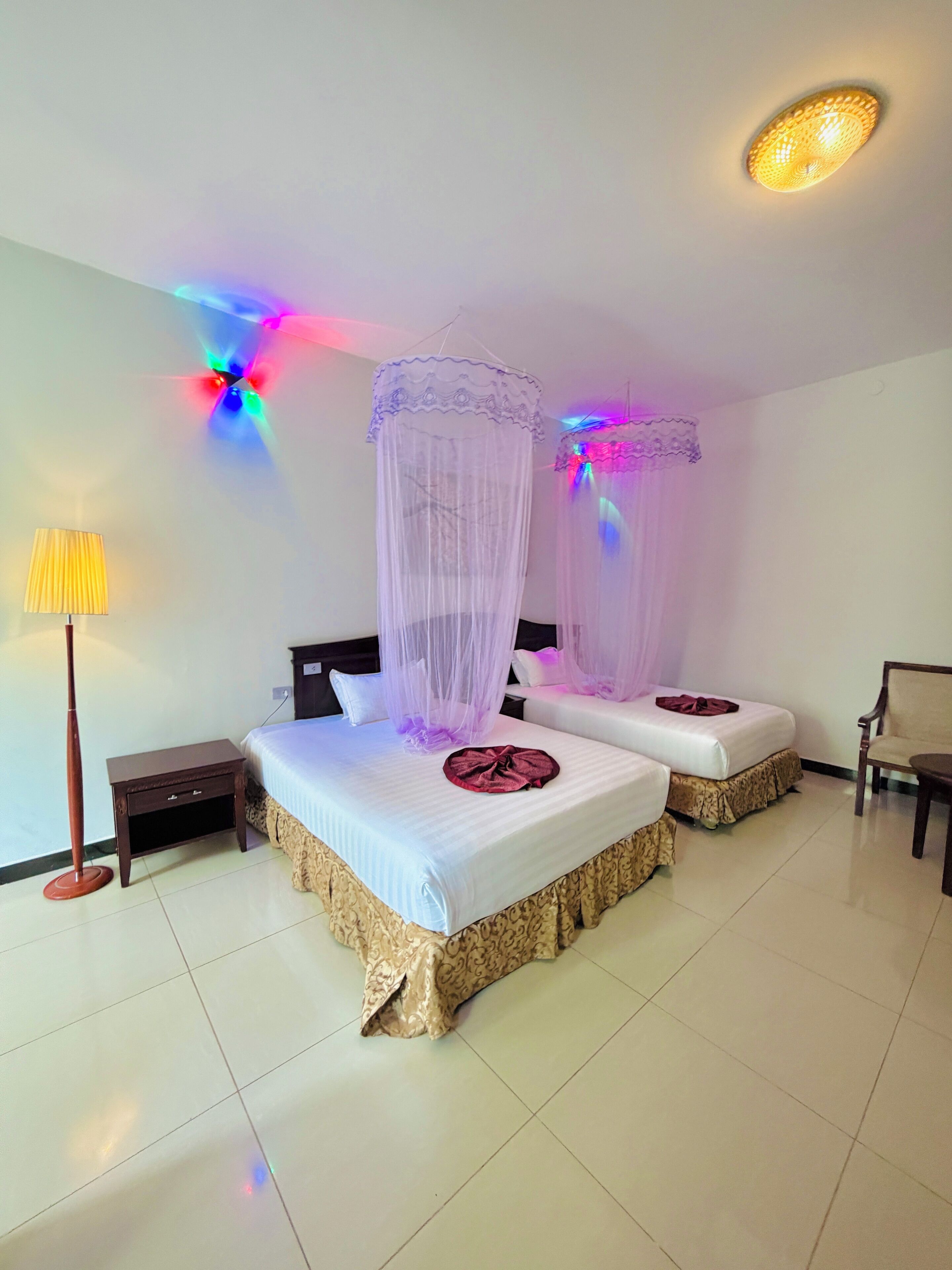 A hotel room with two beds, a bedside table, a lamp, and a ceiling light fixture.