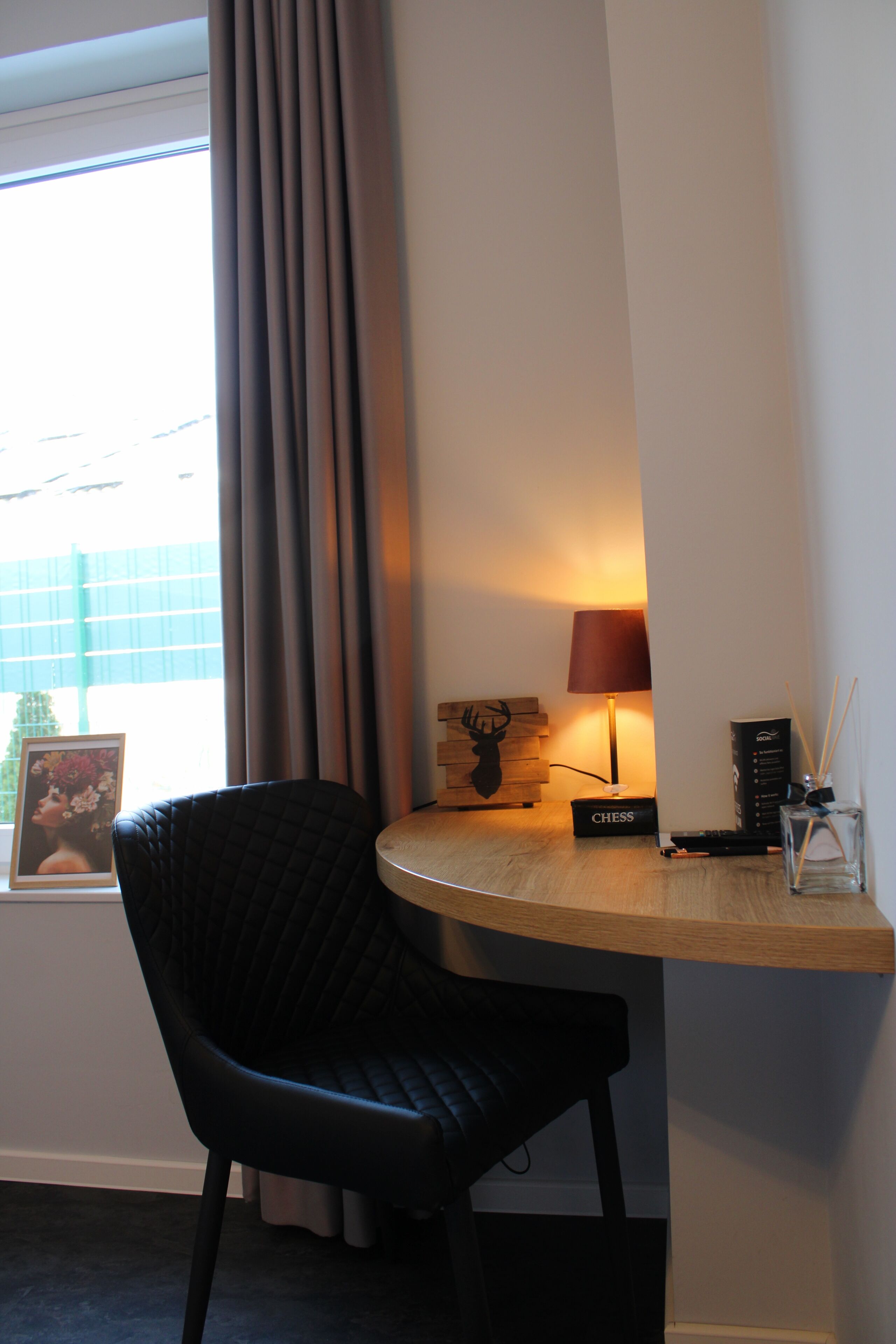 Une pièce d’angle avec une chaise noire, une petite table, une lampe, un jeu d’échecs et un cadre photo.