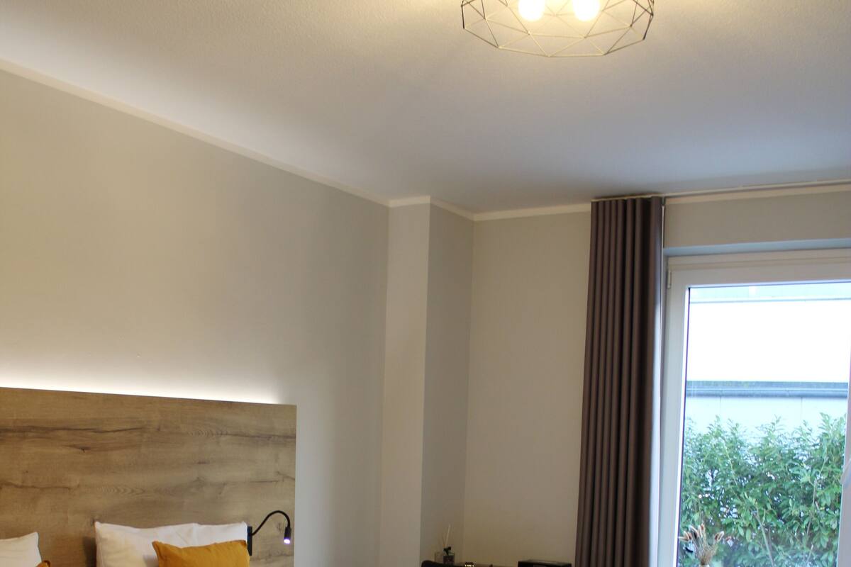 Ein Doppelbett mit Holz-Kopfteil, ein Nachttisch und Blick ins Freie durch ein Fenster.