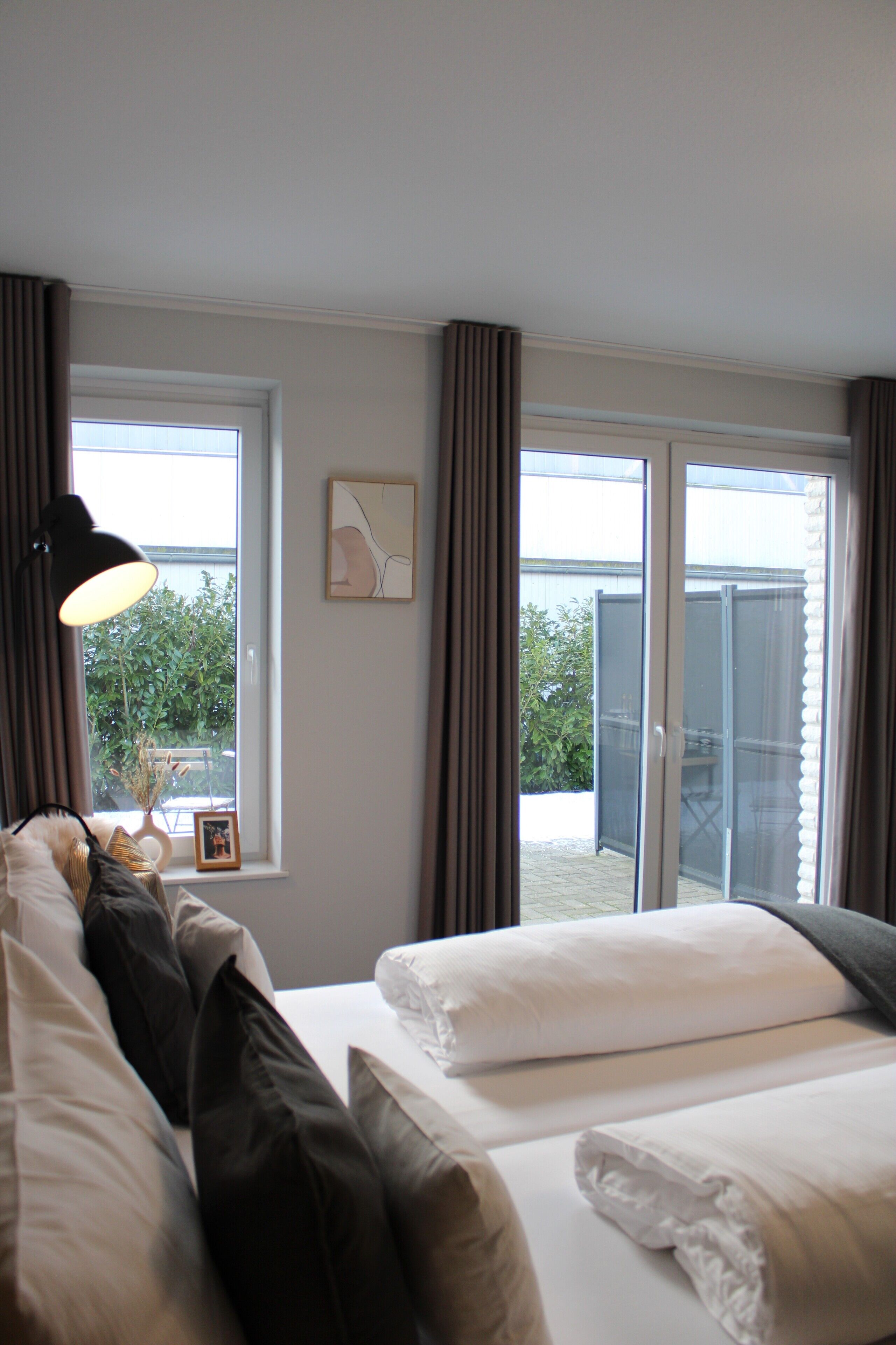A hotel room with two beds, a window with curtains, a framed picture on the wall, and a view of the outside.