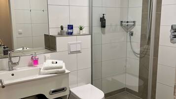A modern bathroom with a glass-enclosed shower, a white sink with a mirror, and a toilet.