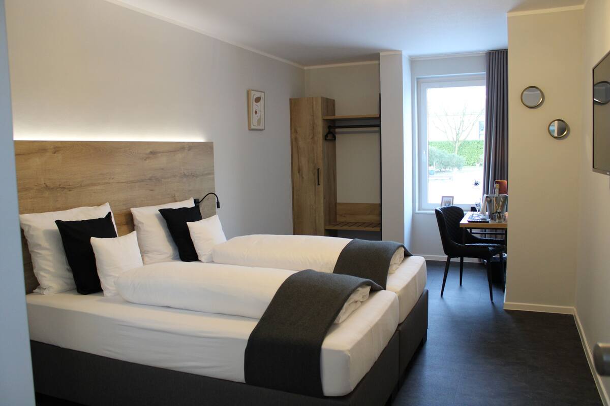 Ein Hotelzimmer mit zwei Betten, einem Holzkopfende, einem Schreibtisch und einem Stuhl.